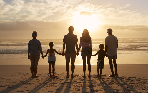 Multigeneration family stands together on the beach during sunset